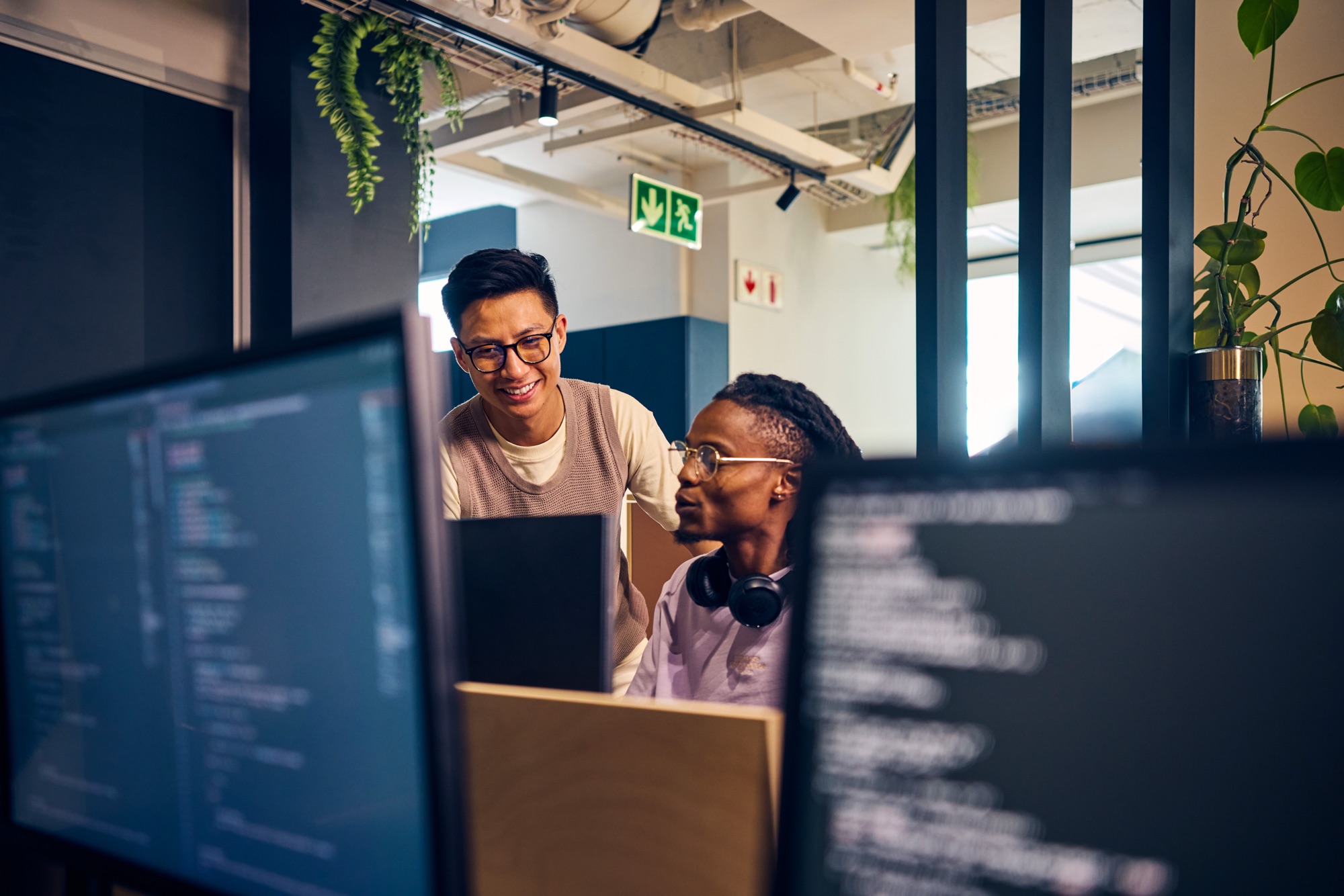 Two developers collaborating at a workstation with code on their screens